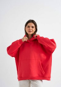 Czerwona, oversize bluza z kapturem, z kieszenią kangurką, ściągaczami przy mankietach i kapturem ze sznurkiem, wykonana z miękkiego, teksturowanego materiału.