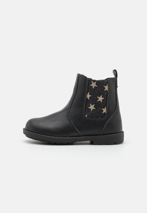 Botas de tornozelo em couro preto com um painel elástico lateral que apresenta estrelas douradas sobre um fundo preto, superfície texturizada e biqueira arredondada.