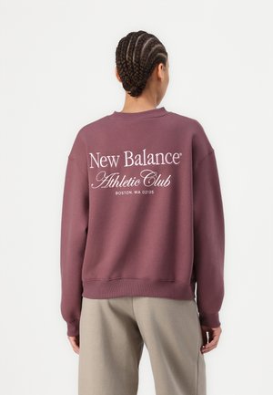 Bordo spalvos megztinis pagamintas iš minkštos medžiagos, su apvaliomis iškirptėmis ir nertomis rankovėmis. Ant nugaros balta spaudinys: "New Balance Athletic Club, Boston, MA."