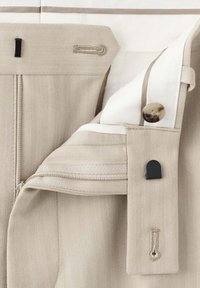 Pantalon en tissu chevrons beige avec fermeture éclair, bouton et ceinture intérieure blanche avec un bouton en marbre marron.