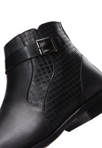 Botín negro de cuero hasta el tobillo con un panel texturizado con un patrón de rejilla, detalle de hebilla lateral y un tacón bajo apilado.