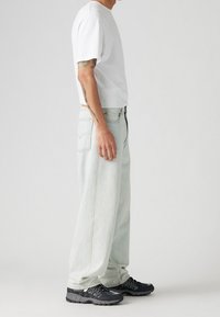 Vit t-shirt med kort ärm, ljusblå vida jeans, svarta sneakers med meshdetaljer. Slät tyg, ledig passform, avslappnad stil.