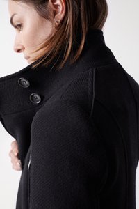 Manteau en mélange de laine noir avec un col haut, doté de grands boutons et d'épaules structurées. Tissu texturé avec des détails de conception sur mesure.