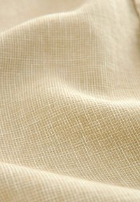 Tissu tissé texturé de couleur beige clair avec un motif en grille, présentant un tombé doux et un éclat subtil.