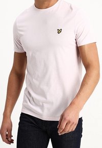 T-shirt rosa chiaro a maniche corte realizzato in cotone, con un piccolo logo ricamato giallo sul lato sinistro del petto e design a collo rotondo.