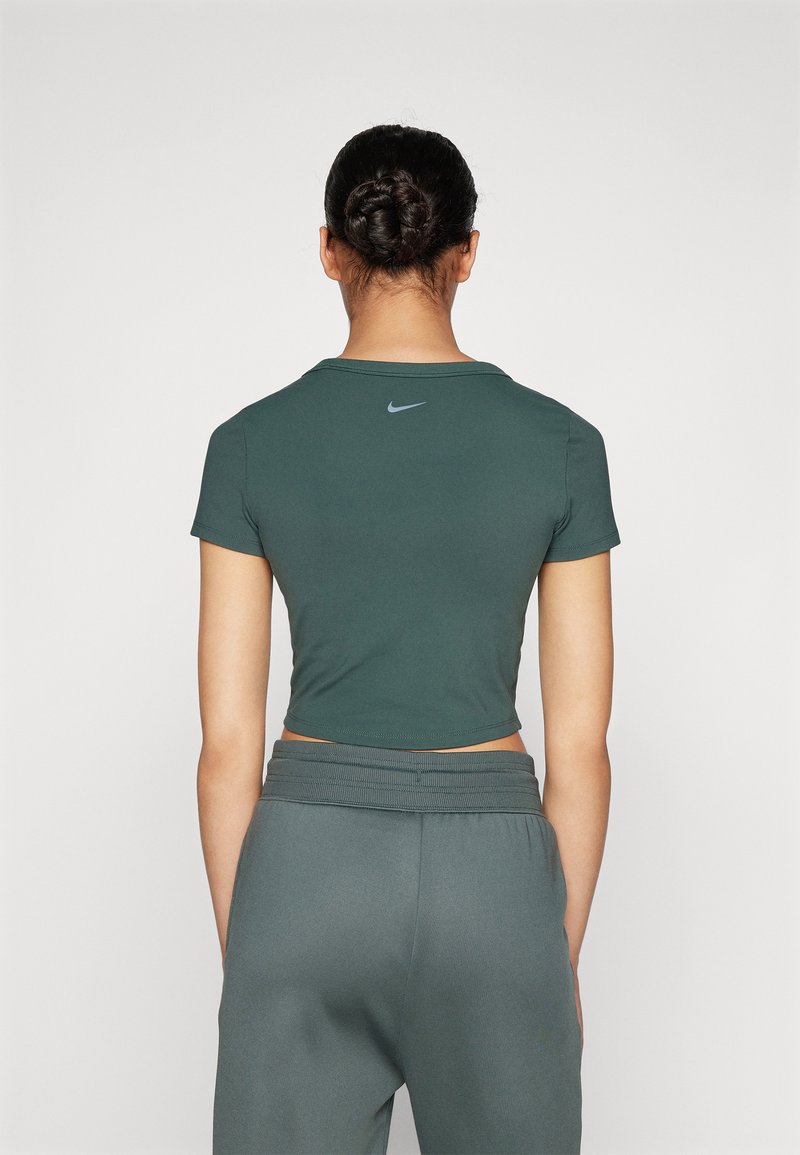 Grüner kurzärmeliger Cropped-Top aus glattem Stoff mit rundem Hals, mit einem kleinen grauen Nike-Logo auf dem Rücken. Kombiniert mit grauen Jogginghosen.