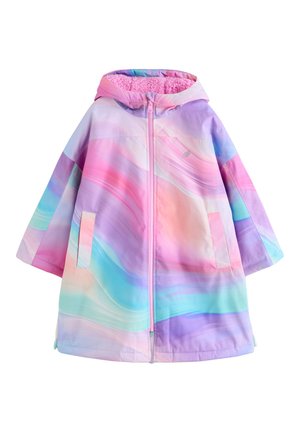 Person iført en pastelrosa, lilla og blå gradientjakke med lynlås foran og hånd stukket ned i sidelomme, der viser fuzzy lyserød ærmekant.