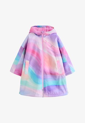 Person iført en pastelrosa, lilla og blå gradientjakke med lynlås foran og hånd stukket ned i sidelomme, der viser fuzzy lyserød ærmekant.