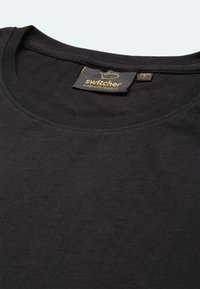 Maglietta nera in cotone con scollo rotondo e dettagli di cucitura sottili. Presenta un'etichetta con "switcher" e "made with respect" stampati in oro.