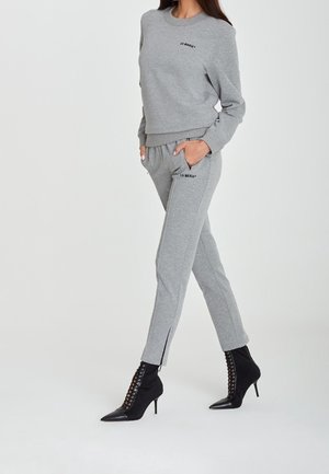 Ensemble en sweat-shirt gris et jogger avec des détails brodés, coupe slim, tissu doux et accents zippés au niveau des chevilles, associé à des bottines noires à talons.
