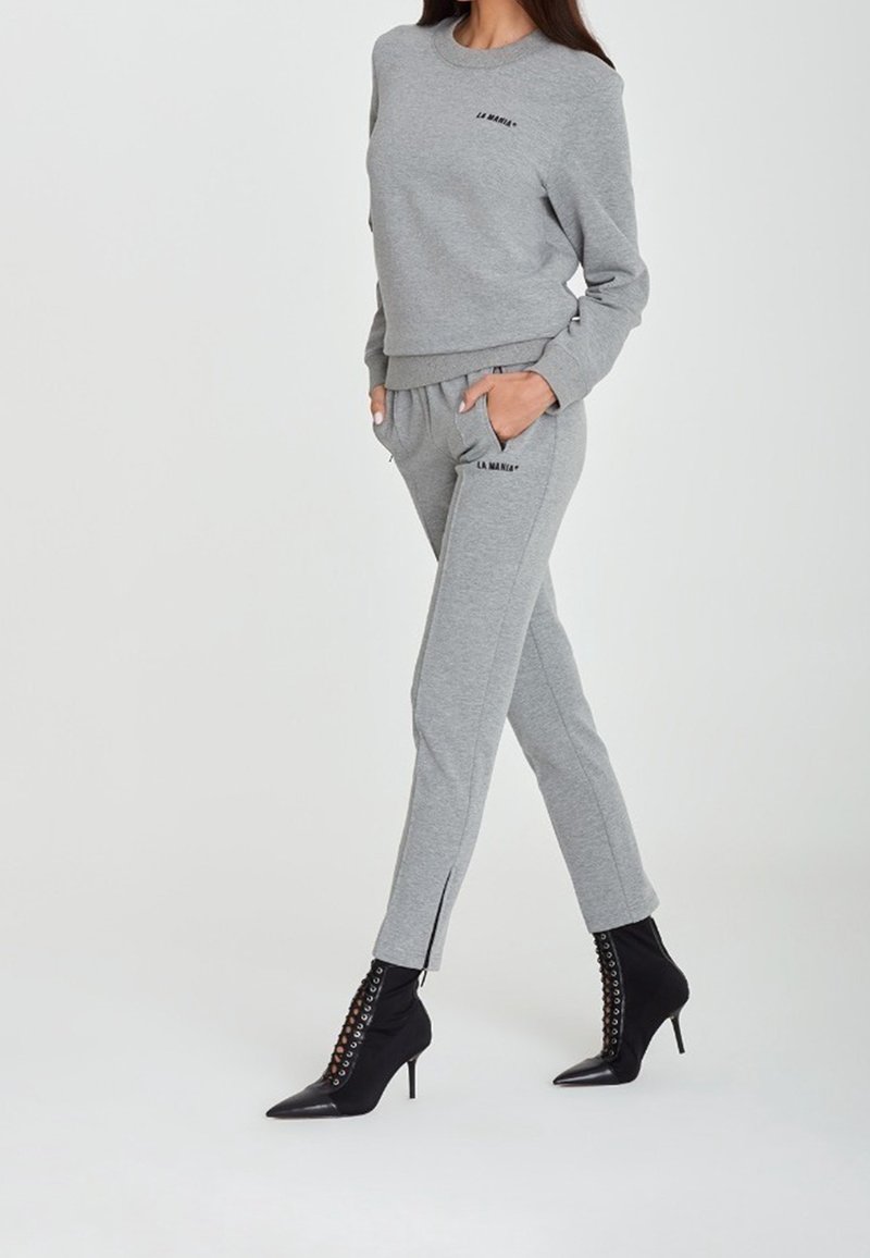 Ensemble en sweat-shirt gris et jogger avec des détails brodés, coupe slim, tissu doux et accents zippés au niveau des chevilles, associé à des bottines noires à talons.