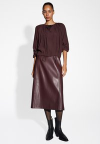 Diep burgundy blouse met geplooide details en een ronde halslijn, gecombineerd met een bijpassende leren midi-rok en enkelboots.