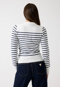 Maglione a righe bianco e blu navy, caratterizzato da una texture a costine, un taglio aderente e un colletto rotondo. La vista posteriore mostra un design morbido con righe a contrasto.