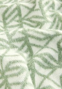 Couverture tricotée avec une texture douce et pelucheuse arborant un motif géométrique de feuilles en vert clair sur un fond crème.