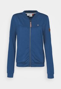 Blå zip-jacka med ribbad krage och ärmslut, med en liten logotyp på ärmen och en dekorativ dragkedja. Slät tygstruktur.