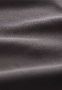 Primo piano di un tessuto grigio scuro, morbido e liscio, con pieghe sottili e una fine trama tessuta visibile in un'illuminazione uniforme.