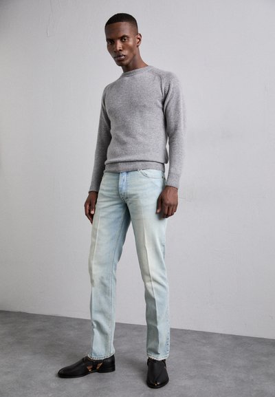 Maglione grigio lavorato a maglia, jeans azzurri chiari con dettagli strappati e scarpe nere. I jeans presentano una vestibilità dritta e un finish sbiadito.