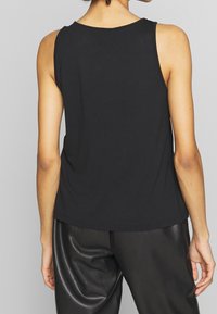 Černý bezramenní top vyrobený z bavlny, s kulatým výstřihem a volným střihem. Tkanina vypadá měkce s minimem švů.