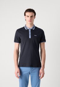 Črna polo majica z strukturiranim ovratnikom, ki ima svetlo modre črte, tri gumbe in majhen bel logotip na prsih. Kratke rokave.