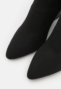 Mustad mustasaapad tekstureeritud kangast, terava varbaga. Pinna peal on peen mesh-muster, mis täiendab üldist disaini.