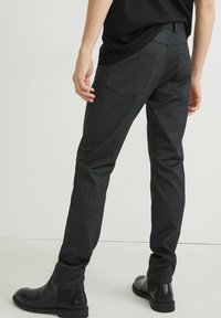 Tmavě šedé kalhoty z texturované tkaniny se štíhlým střihem, dvěma zadními kapsami a páskem v pase, doplněné černými botami.