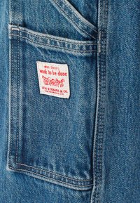 Denim fabric, light blue color, features a red and white label reading "when there's work to be done," with stitching details visible.
