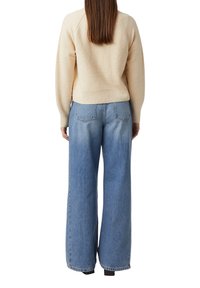 Kremowy sweter o teksturowanej powierzchni z dopasowanym dołem oraz szerokie niebieskie dżinsy z tylnymi kieszeniami i przetartym efektem. Mankiety są lekko wydłużone.