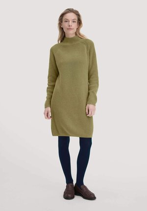 Abito in maglia verde oliva con collo alto e maniche lunghe, abbinato a collant blu navy e mocassini marrone scuro. Presenta un motivo testurizzato.