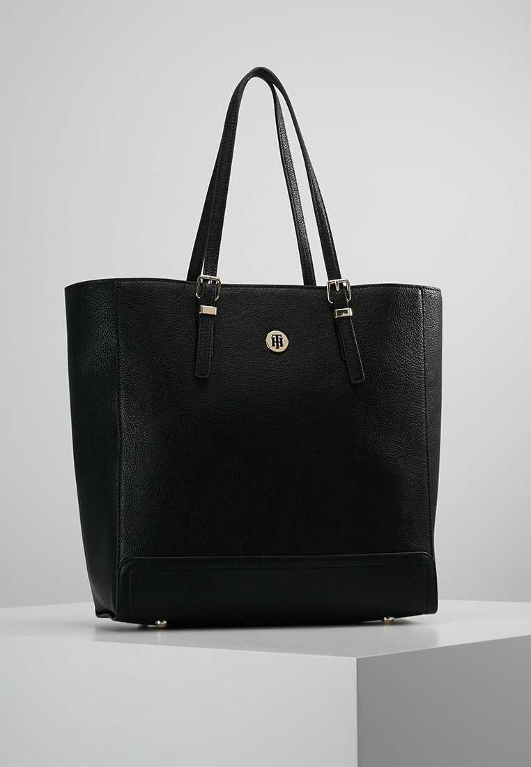 Sac cabas en cuir noir à forme structurée, avec deux poignées supérieures, quincaillerie dorée et un logo en relief à l'avant.