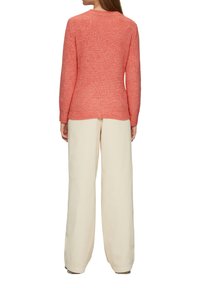 Sweter zrobiony na drutach w kolorze koralowym, z teksturowanym wzorem, okrągłym dekoltem i długimi rękawami, zestawiony z kremowymi spodniami w szerokim kroju.