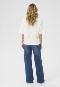 White short-sleeve top paired with high-waisted blue wide-leg jeans. The top has a smooth texture, and the jeans feature subtle pocket stitching.