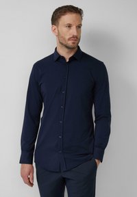 Chemise boutonnée bleu marine à manches longues, col pointu et coupe ajustée. Fabriquée en tissu doux et lisse avec un subtil éclat.