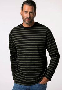 Langärmliges Shirt mit schwarzen und olivgrünen horizontalen Streifen, runder Ausschnitt, weicher Stoff und lockere Passform. Denim-Jeans sind auf Taillenhöhe sichtbar.