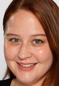 Fokusert nærbilde av et ansikt med rett, skulderlang rødbrun hår, blå øyne, klar hud og et subtilt smil. Jevn tekstur og lett sminke.