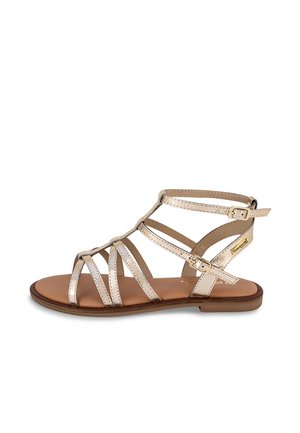 Sandalia gladiadora de tiras en dorado metálico con múltiples tiras estrechas, hebilla ajustable y suela plana marrón. Forro interior suave.