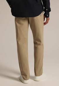 Beżowe bawełniane chinosy o prostym kroju, z subtelnymi tylnymi kieszeniami i gładką fakturą, w połączeniu z białymi trampkami i granatową koszulą.