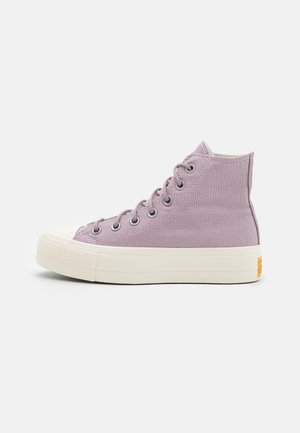 Lila højtop canvas sneakers med hvid tyk gummisål og hvid tåhætte, set fra siden på en ensartet, lys baggrund.