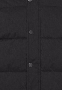 Svart puffervest med quiltet design, metall trykknapper og en strukturert stoffoverflate.