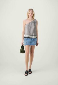 Top asimétrico de un solo hombro en tejido estampado, combinado con una minifalda de mezclilla, sandalias negras de dedo abierto y un bolso verde.