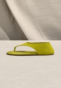 Πλατφόρμα σανδάλι σε φλατ στυλ με λουράκι lime πράσινο, κλειστή φτέρνα και λεπτή σόλα, τοποθετημένο σε ανοιχτό φόντο πάνω σε ουδέτερο ύφασμα.