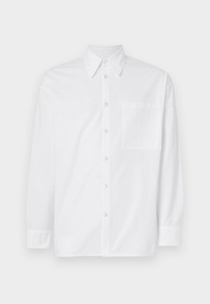 Camisa branca de mangas compridas feita de algodão. Possui um colarinho clássico, fecho frontal com botões e um único bolso no peito do lado esquerdo.