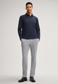 Polo shirt a maniche lunghe blu marino con motivo a diamante, abbinato a pantaloni slim-fit grigi chiari e stivali di pelle neri.