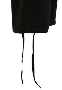 Svarta tygshorts med en texturerad yta, med en fåll ovanför knäet och två långa svarta dragsko som hänger neråt.
