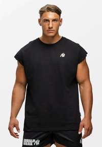 Zwarte mouwloze T-shirt van katoen, met een ronde hals en rafelige armsgaten. Een klein wit gorilla-logo op de borst.