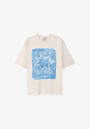 Beżowy T-shirt z krótkim rękawem z niebieskim kwadratem przedstawiającym uśmiechającą się gwiazdę i napisem "PATRZ NA MÓJ VIBE" z przodu.