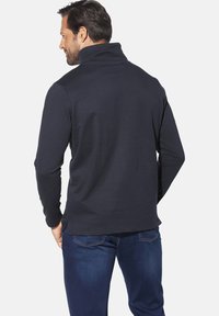 Navy pullover with a high collar, featuring long sleeves and a smooth texture. Paired with denim jeans, showcasing a casual look.