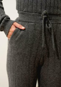 Šedé žebrované pletené tepláky s nastavovacími šňůrkami v pase a bočními kapsami, s měkkou texturou a uvolněným střihem.