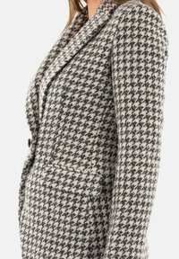 Blazer su misura in un motivo a scacchi bianco e nero, con colletto a reversing, tasca frontale e tessuto testurizzato con una leggera lucentezza.