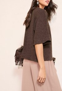 Pruun lühikeste varrukatega kampsun lõdva istuvusega, kombineeritud voolava, heledapunase alaosaga ning tumeda kotiga, millel on tuttide detailid.