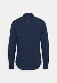 Chemise bleu marine à manches longues avec un petit motif à pois blancs et rouges, poignets boutonnés et une petite étiquette en tissu dans le haut du dos.